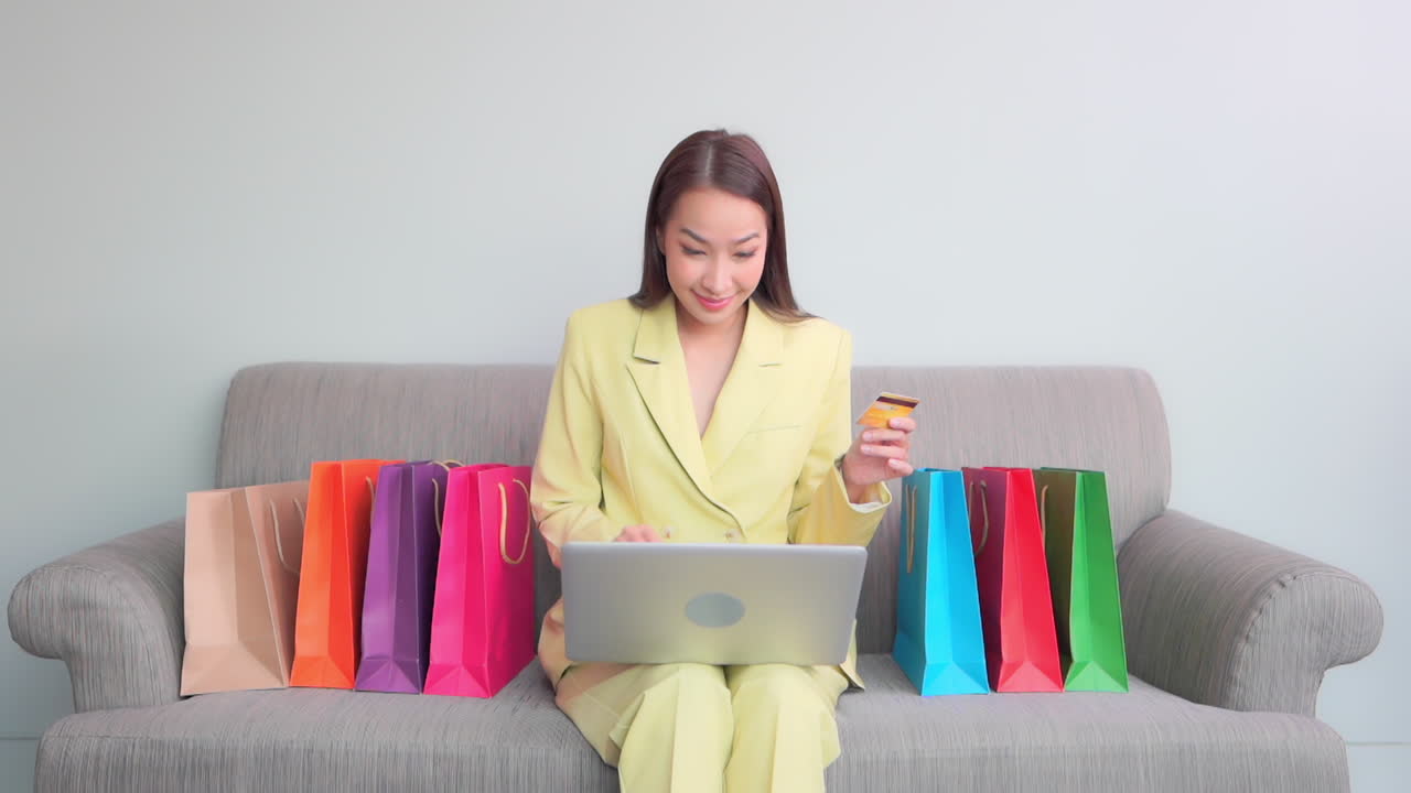 joven asiática sentada en un sofá usando una computadora portátil comprando en línea con tarjeta de crédito comprando en internet, obteniendo descuento o ganando lotería, gesto de mano ganadora