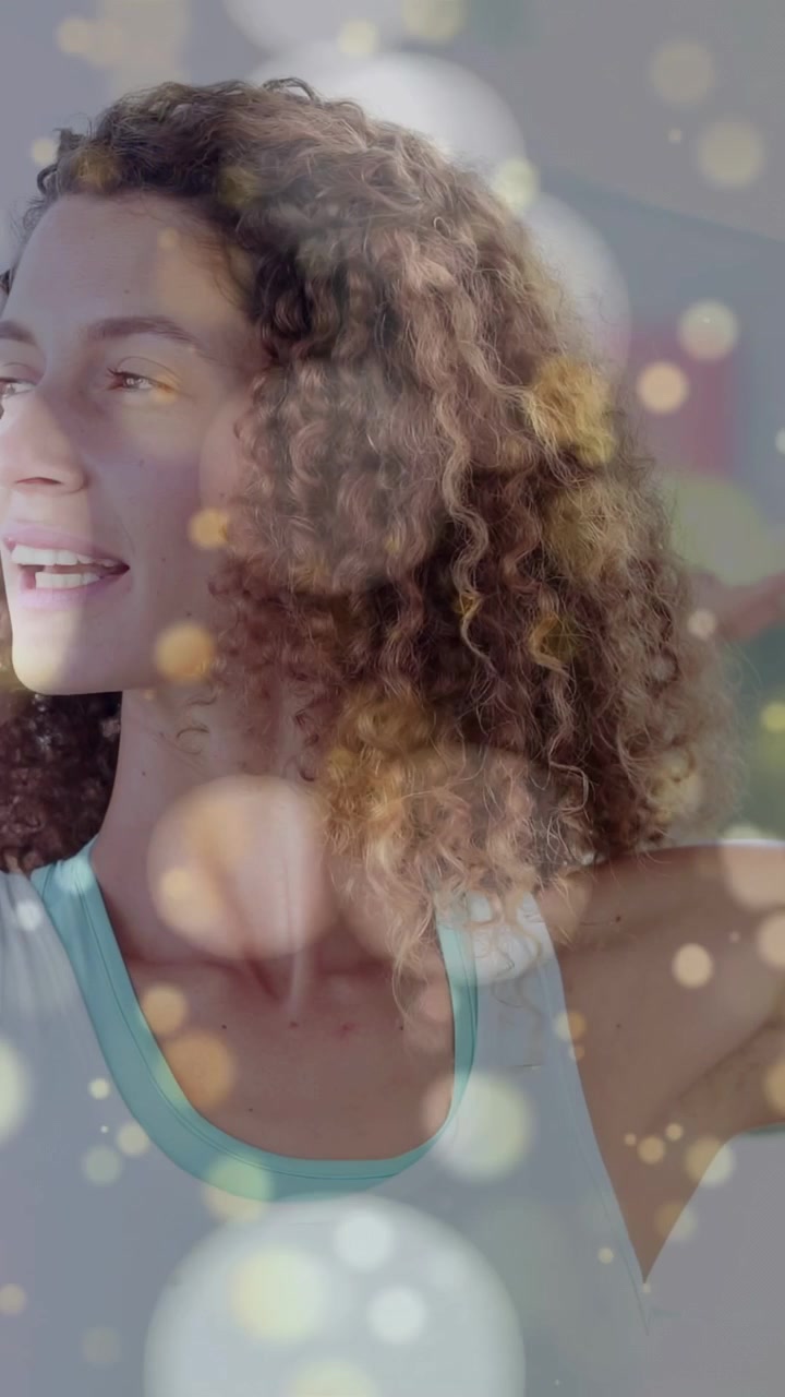 Vertical video: Woman doing fitness warmup, pressing palms reaching back while bokeh overlaying her