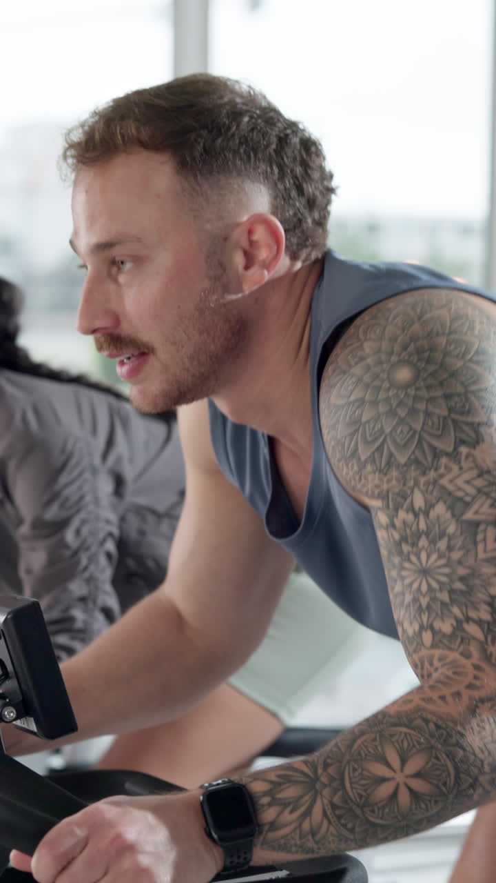 Hombre con tatuajes pedaleando en bicicleta estática en un gimnasio