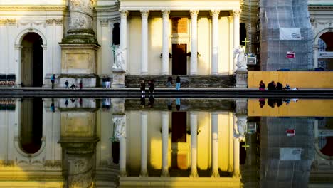 reflections of vienna's karlskirche in a calm pool, capturing evening light and passing people, timelapse