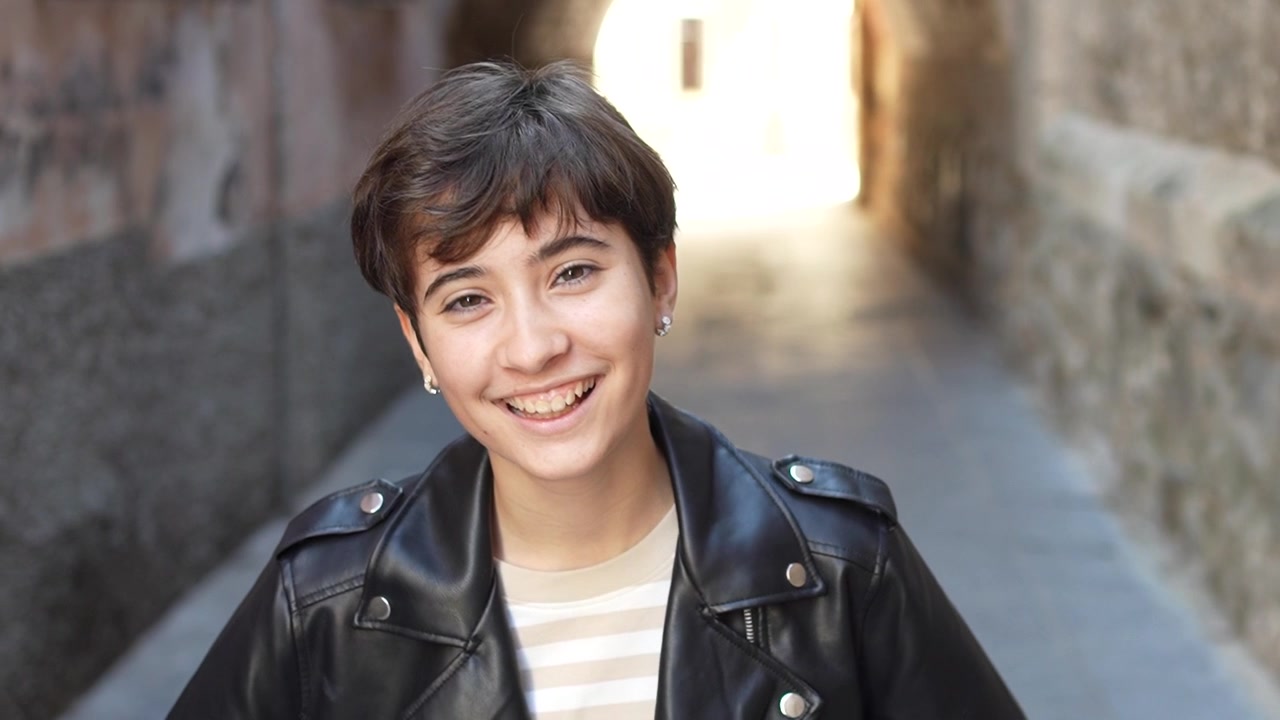 A cheerful young individual is smiling brightly in a vibrant urban alleyway environment
