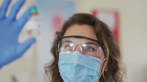 maestra con máscara facial y gafas protectoras sosteniendo una botella de vial en el laboratorio