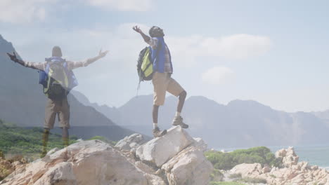 composite of happy african american man hiking, and raising arms on mountainside