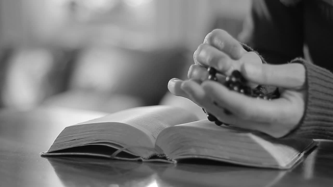 Hands holding a rosary over an open religious book, symbolizing prayer and devotion