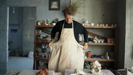 young happy potter starts his working day. the creator puts on and apron and glasses