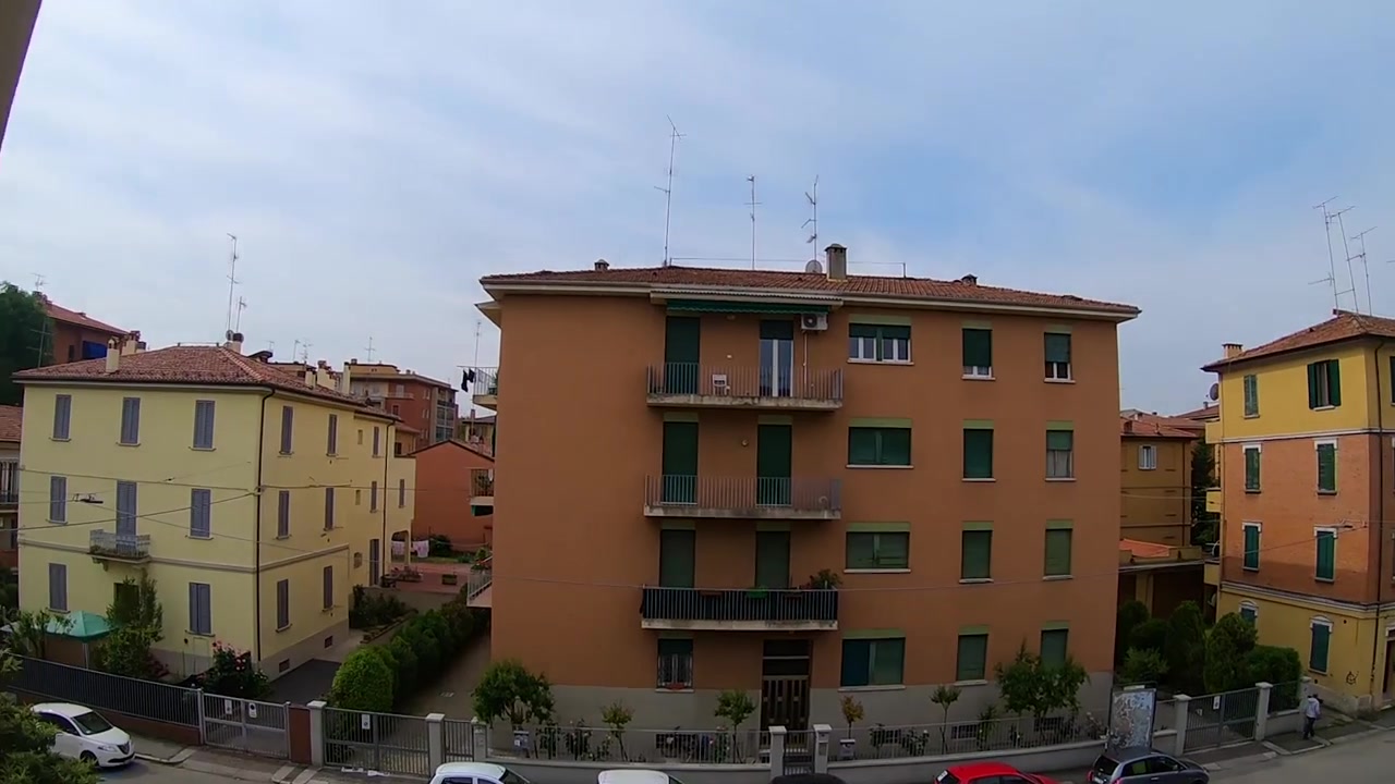 Una camminata costante e fluida attraverso una camera d'albergo, passando accanto a un letto vintage e poi entrando nel balcone, con una vista in una giornata di sole di alcuni edifici dall'altra parte della strada