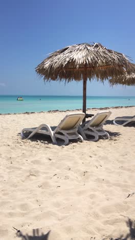 Sandstrand-Und-Strohschirme-In-Varadero,-Kuba-Mit-Sonnenliegen-Und-Blauem-Meer,-Nicht-Erkennbare-Personen,-Vertikales-Video