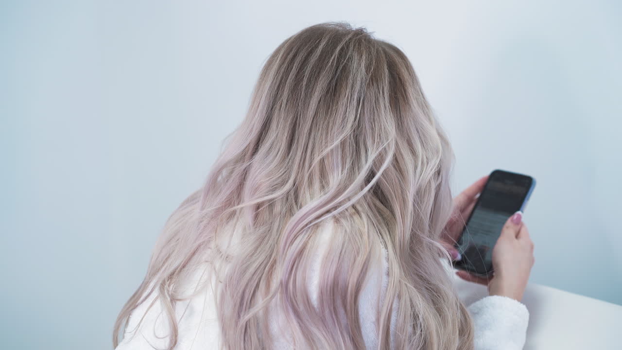 레이저 탈모를 하고 있는 여성이  ⁇ 드폰으로 인터넷을 서핑하고 있습니다.