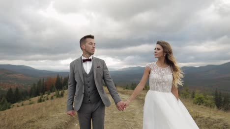 Lovely-caucasian-wedding-newlyweds-family-bride-groom-holding-hands,-making-a-kiss-on-mountain-slope