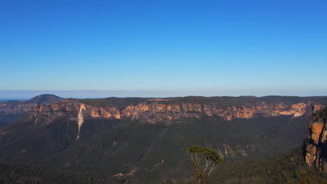 Ascending-drone-rising-to-rock-outcrop-covered-in-trees-and-bushes-in-the-Blue-Mountains-clear-blue-sky-in-New-South-Wales