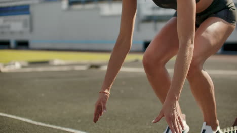 slender young girl athlete is in position to start running in the pads on the track in slow motion