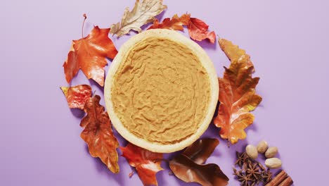 video of autumn leaves, spices and pie on purple background