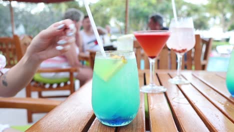 person stirring a blue cocktail on a wooden table