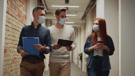 hombres y mujeres de negocios caminando hacia la cámara durante la pandemia de covid-19. personas con máscaras faciales van a una reunión de trabajo.