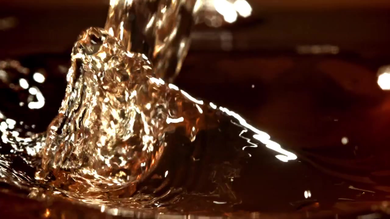 Primo piano al rallentatore di liquido dorato che si versa in una bevanda scura