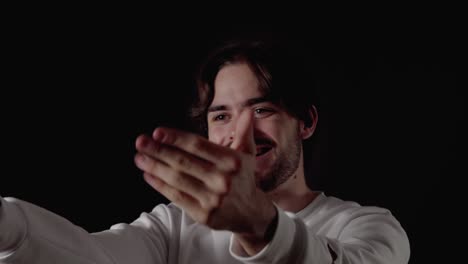 trendy young man welcoming camera, waving gesture, close, black background