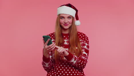 Frau-Im-Weihnachtspullover-Schaut-Auf-Smartphone-Display-Und-Freut-Sich-Aufrichtig-über-Erfolg-Und-Glück,-Daumen-Hoch