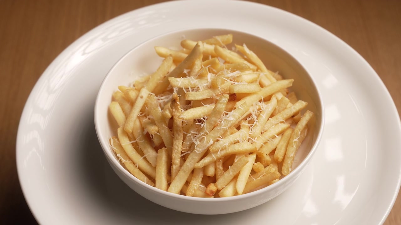 Delicious crispy golden french fries topped with grated parmesan cheese in a white bowl