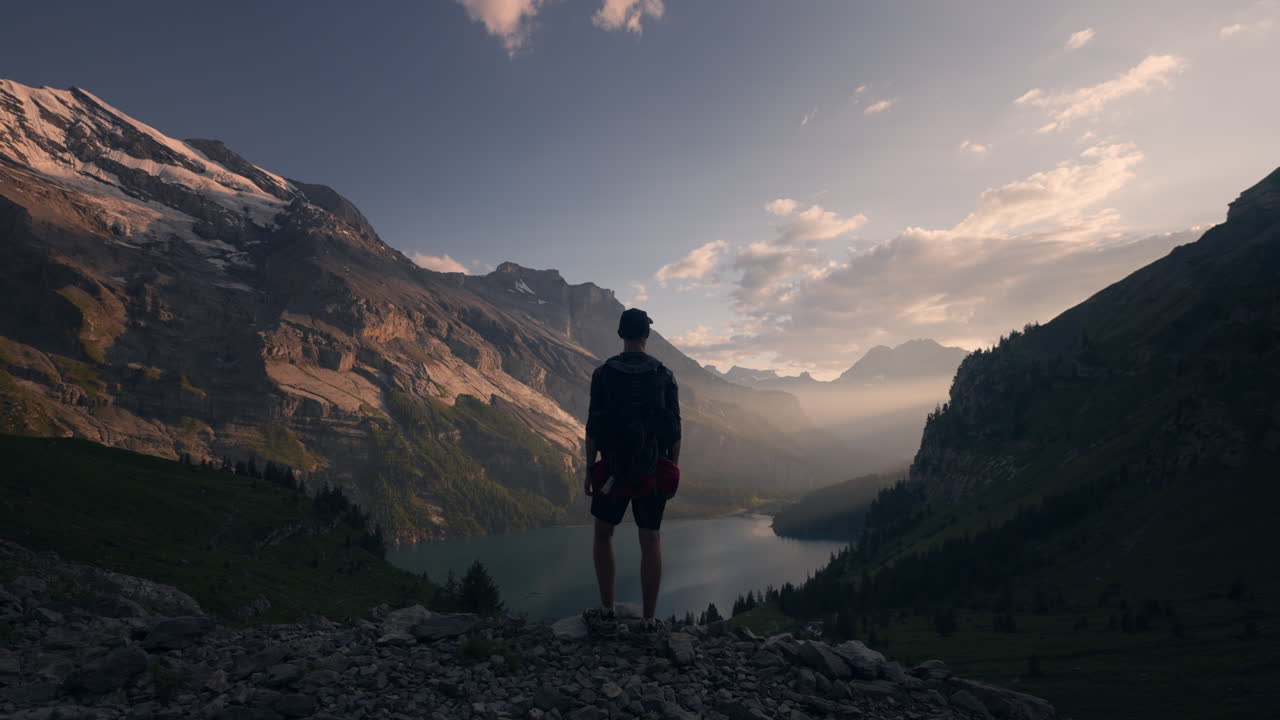 Man standing on mountain peak overlooking a Swiss valley lake during sunset