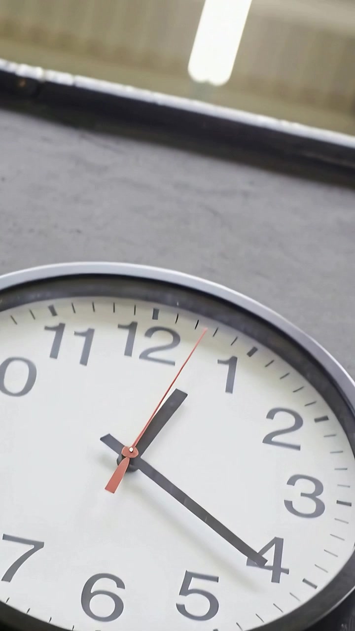 Video vertical: Cámara inclinándose para revelar un reloj analógico en un taller, con un tubo encima y el segundero moviéndose.