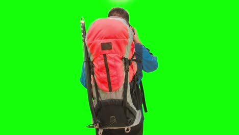 An-adult-tourist-with-a-backpack-stands-in-a-green-screen-studio,-holding-a-camera