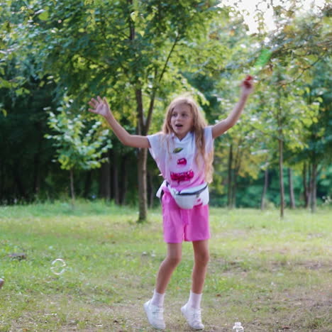 happy girl playing with bubble blower in the park. beautiful child jumping joyfully waving wand with soap bubbles on the natural background.