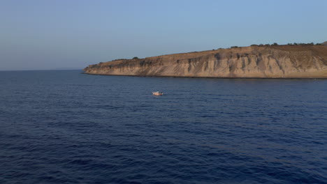 Aerial:-Tracking-shot-of-one-small-boat-sailing-near-the-shore-during-sunset