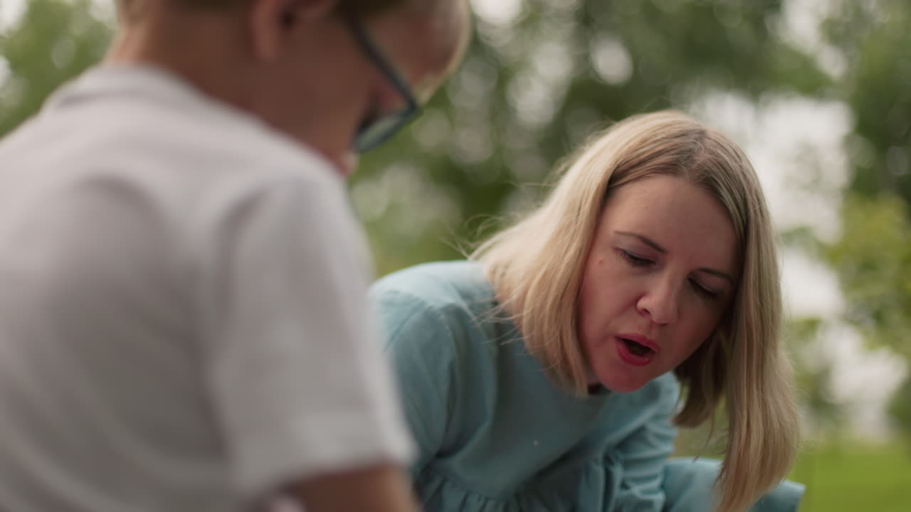 파란 드레스를 입은 여자가 무언가에 공기를 고 있는 모습이 보이며, 안경을 입은 아이의 흐릿한 모습이 배경에 나타납니다.