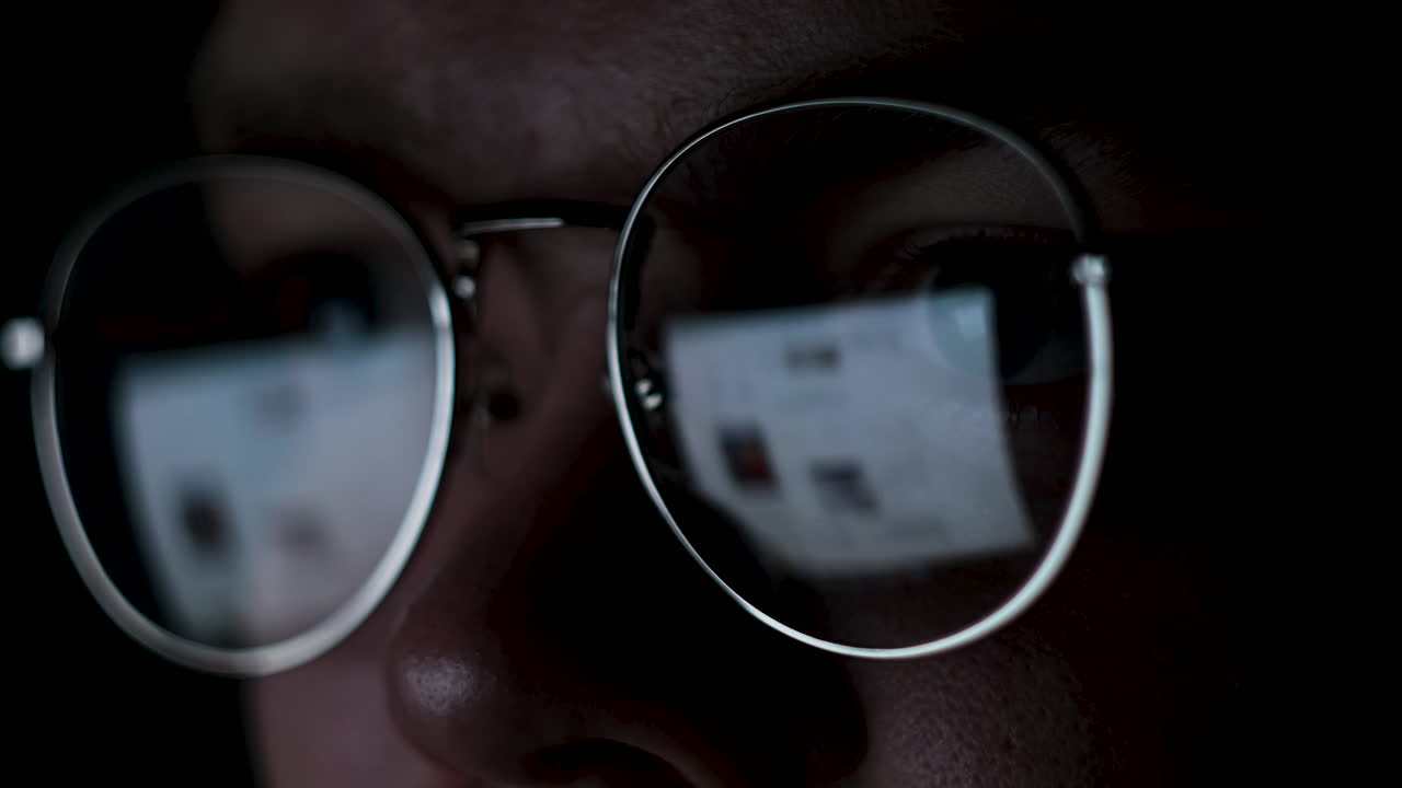 persona con gafas mirando una pantalla de computadora por la noche