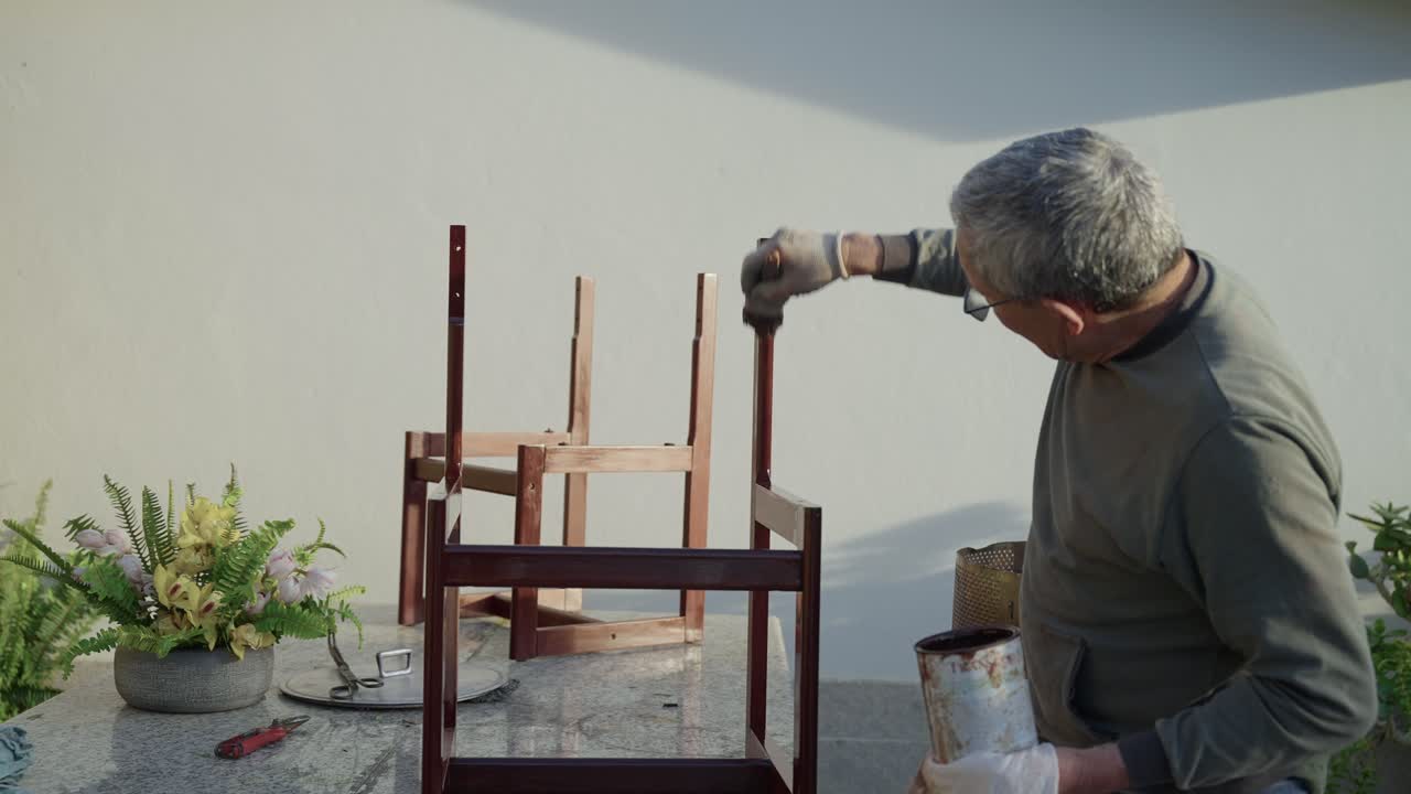 Man applying varnish with brush to wooden chair frame placed on table outdoors