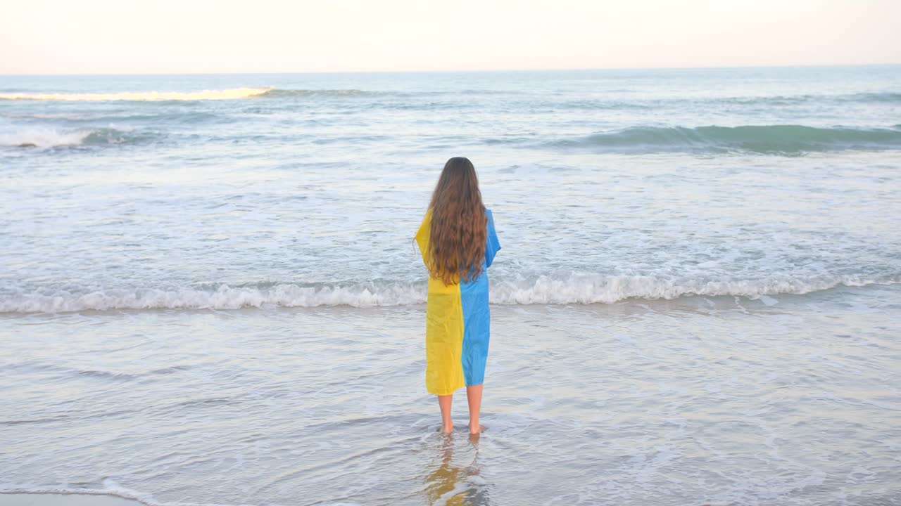 해안으로 압연 바다 파도를보고 그녀의 뒤에 우크라이나 국기를 들고 곱슬 금발 머리를 가진 어린 소녀