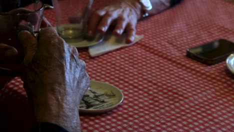 Cerca-De-Las-Manos-De-Un-Anciano-Sosteniendo-Una-Taza-De-Té-Caliente-Mientras-Habla-Con-Su-Hija-En-La-Mesa-Del-Desayuno