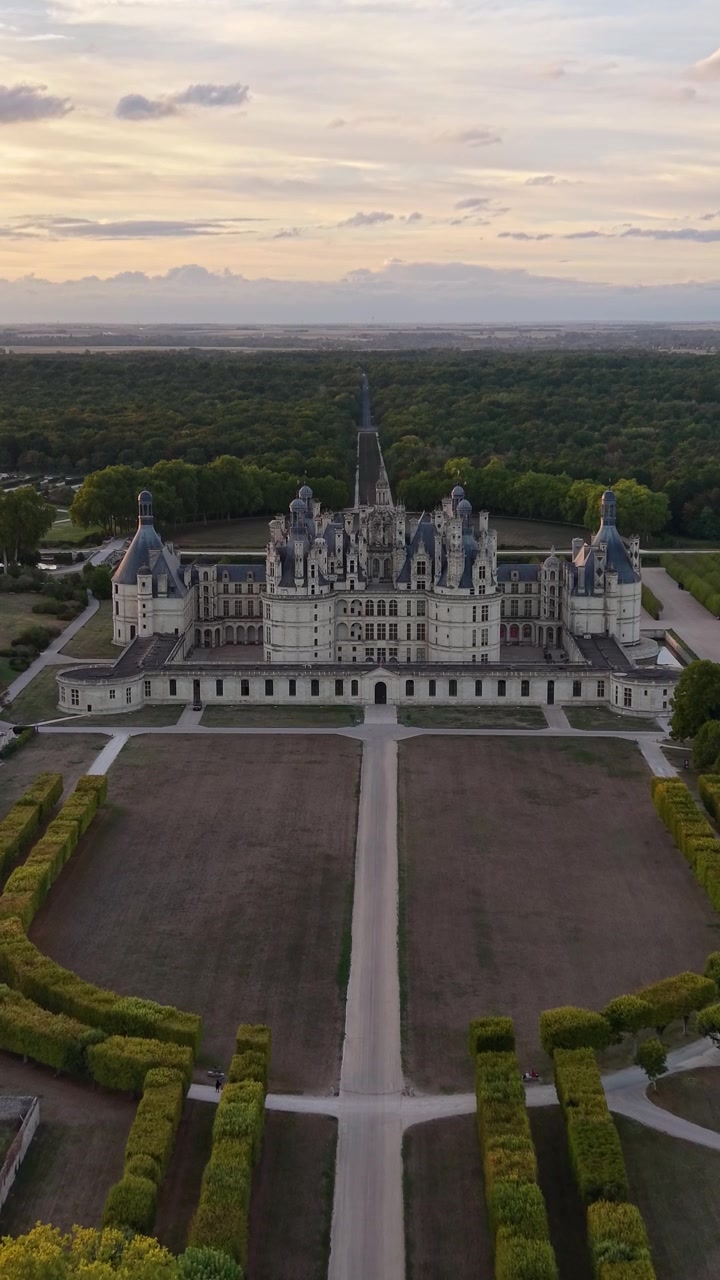 Riprese aeree cinematografiche del Castello di Chambord che rivelano la sua facciata rinascimentale simmetrica, i giardini formali, l'asse centrale e il bosco circostante al tramonto