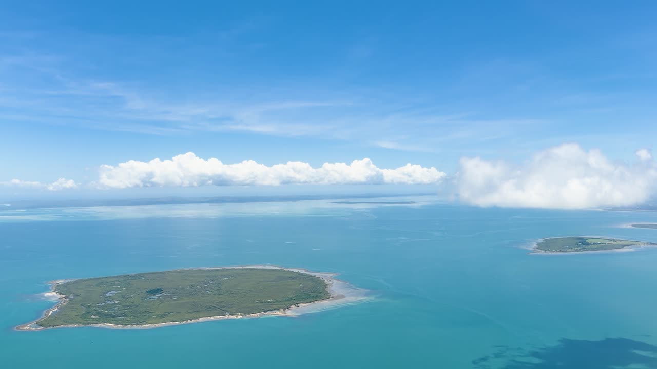 Smooth aerial flyover of small green islands in turquoise ocean under bright blue sky