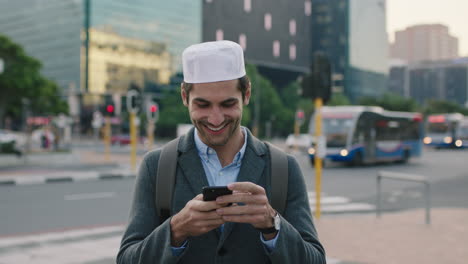 Primer-Plano-Retrato-De-Un-Joven-Musulmán-Atractivo-Enviando-Mensajes-De-Texto-Navegando-Usando-La-Aplicación-De-Mensajería-Móvil-Para-Teléfonos-Inteligentes-En-Las-Calles-Urbanas-De-La-Ciudad