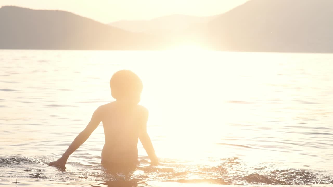 행복한 아이는 해가 지면 바다에서 수영합니다. 즐거운 소년은 놀고 호수에서 수영하는 동안 물로 어집니다. 학교 휴가 동안 활발한 여가