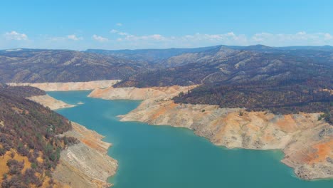 Inquietante-Antena-Sobre-El-Lago-Oroville-De-California-Azotado-Por-La-Sequía-Con-Bajos-Niveles-De-Agua,-Costa-En-Retroceso-Y-Gran-Cruce-De-Puentes