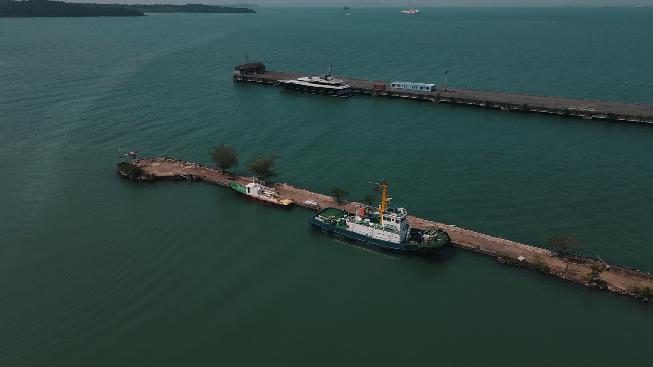 항구 예인선과 파일럿 보트는 시아누크빌 항구의 석조 부두에 정박해 있으며 호화 여객선은 배경에 놓여 있습니다.