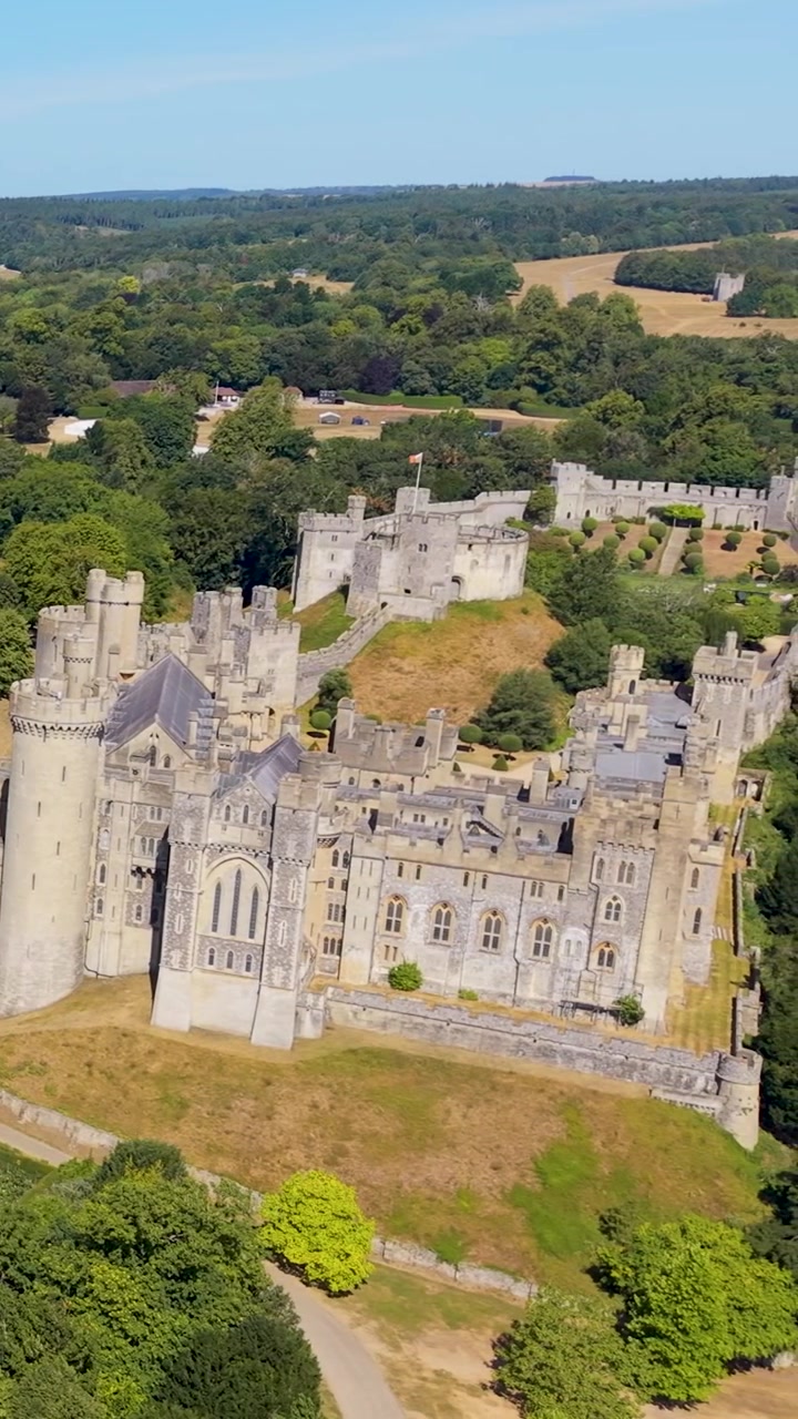 Panoramique aérien d'Arundel sur la ville, révélant le château d'Arundel à droite. Toits historiques, cathédrale et parcs verdoyants dans le West Sussex, Angleterre, sous un ciel d'été dégagé. Format vertical