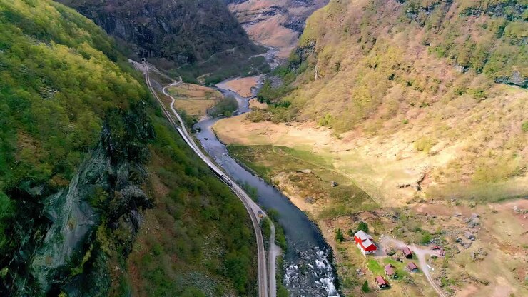 Un fiume che scorre attraverso una valle ripida con un treno sui binari della ferrovia - vista aerea