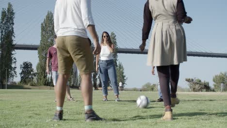 group of five happy friends kicking ball in park.