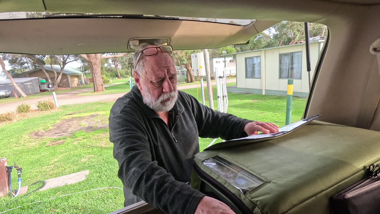 Um campista retira comida de uma geladeira de carro enquanto desfruta de um dia em um acampamento cercado pela natureza e atividades ao ar livre.