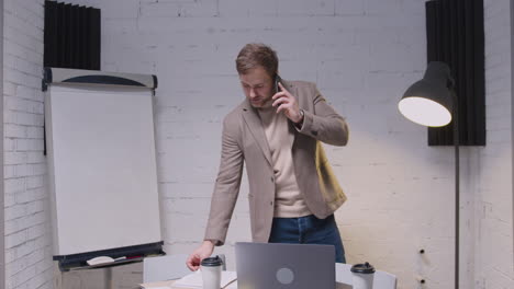 busy businessman talking on mobile phone and checking information on laptop computer in the office