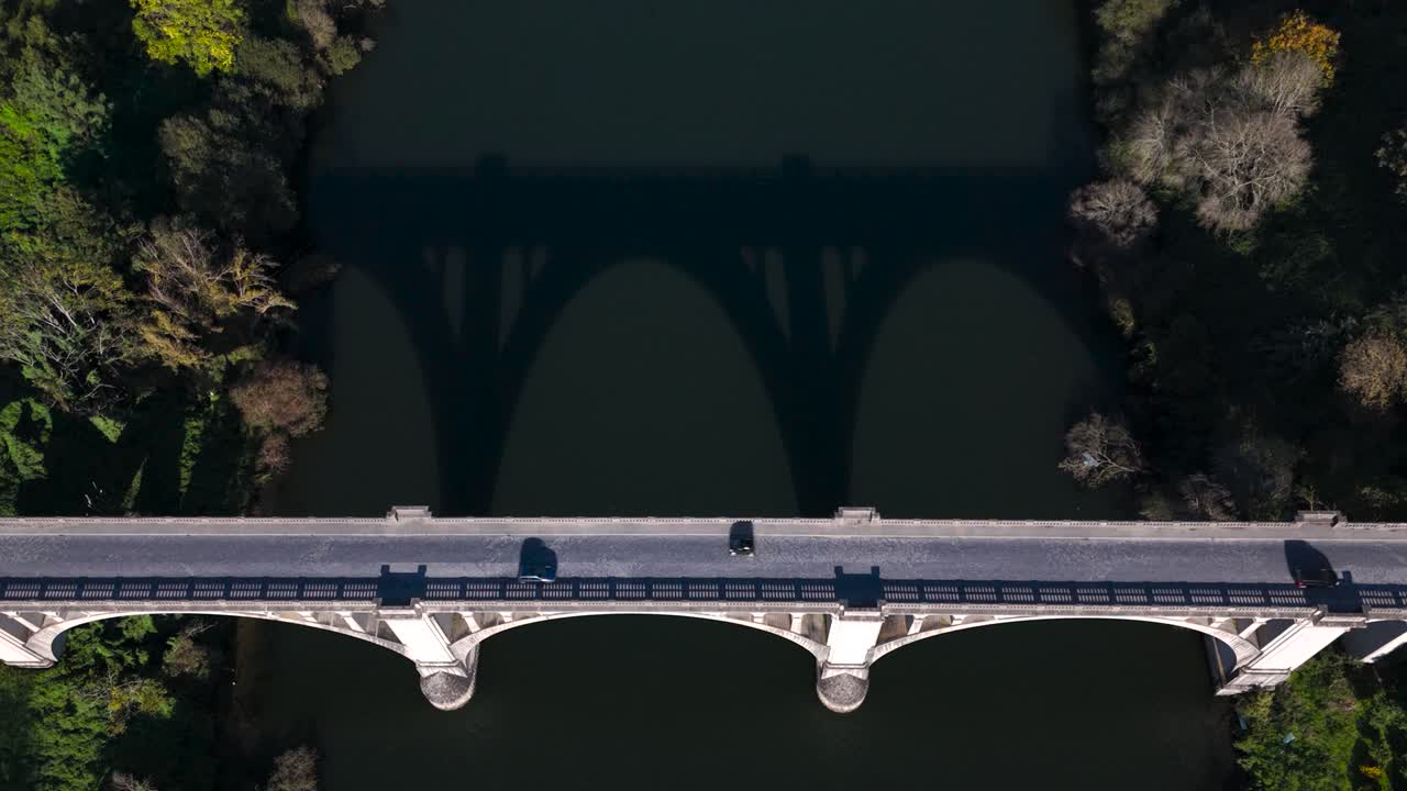 stone arch bridge with cars passing by and aesthetic shadow in the river, still aerial drone view