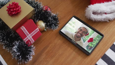 hombre biracial sonriente con sombrero de santa en una videollamada de navidad en una tableta