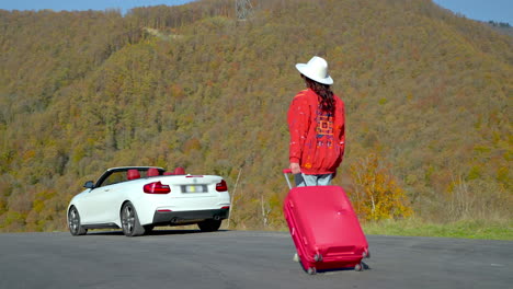 mujer con una maleta cerca de un coche convertible en las montañas durante el otoño