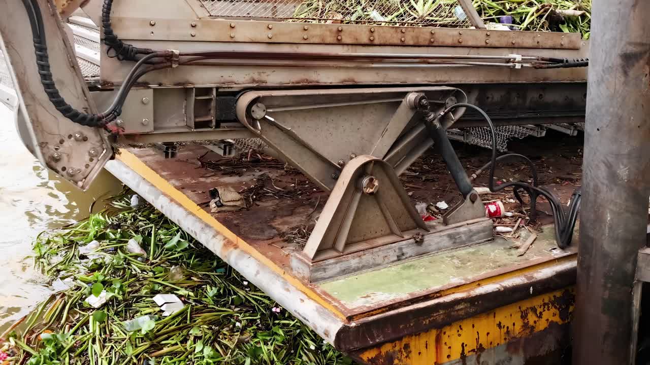 A close-up view of a mechanical arm gathering floating vegetation from a river surface.