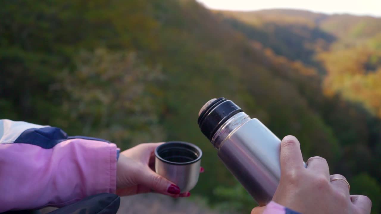 pouring up coffee from a thermos while watching a beautiful valley with beech forest.