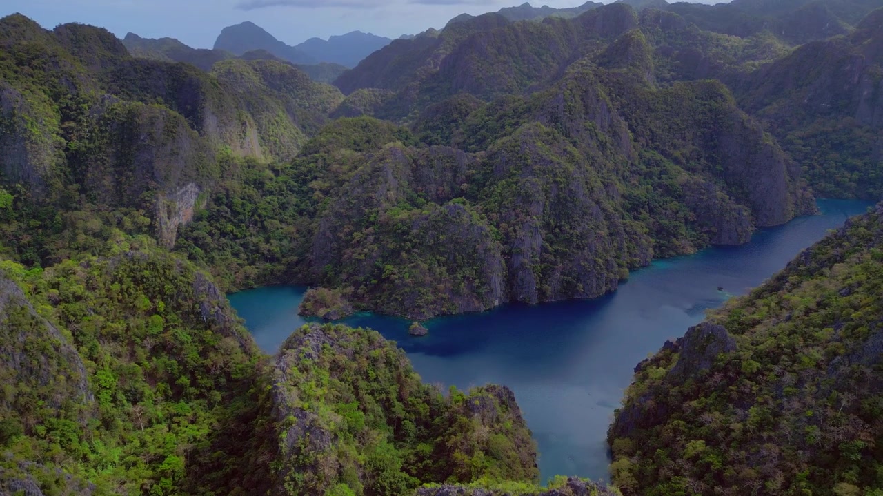 Água turquesa do Lago Kayangan, uma lagoa escondida cercada por imponentes carstes de calcário cobertos por vegetação verde exuberante. Vista aérea única em panorama de drone ascendente.