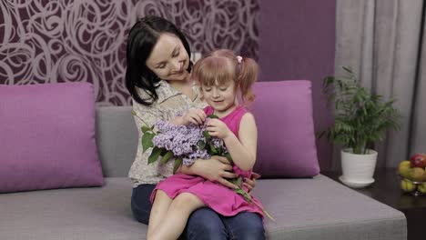 Little-daughter-and-mother-sitting-on-sofe-with-bouquet-of-lilac-purple-flowers